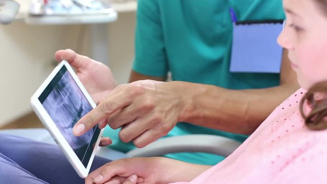 Assistant showing cute little girl dental X- ray on tablet, closeup