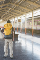 Young man walking on the station platform with backpack on train station
