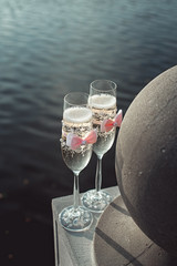 Two wedding champagne glasses with a bow on a stone railing. Lake promenade at sunset