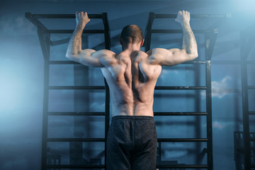 Strong sportsman training on horizontal bar in gym