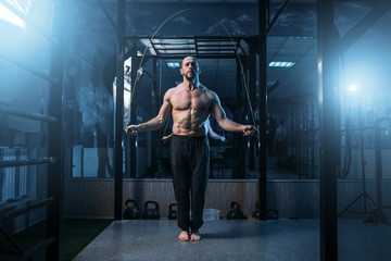 Muscular athlete exercises with jump rope in gym