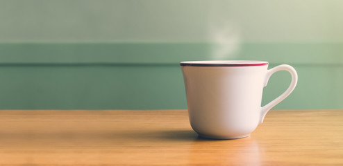 Vintage filter,Hot white coffee cup on wood table with blur pastel green wall with sun light from right side,Leave copy space for adding your text or design
