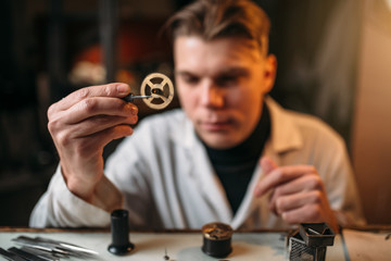 Watchmaker holding with tweezers a gear of hours