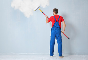 Young worker painting wall in room