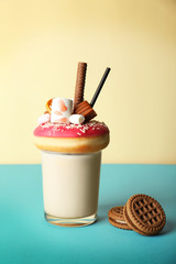 Milkshake, donut and other sweets in glass on color background