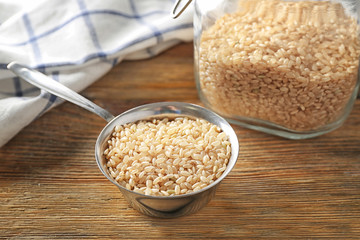 Metal measuring cup with brown short grain rice on wooden table