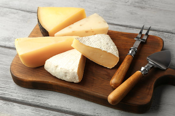 Board with delicious cheese on wooden table
