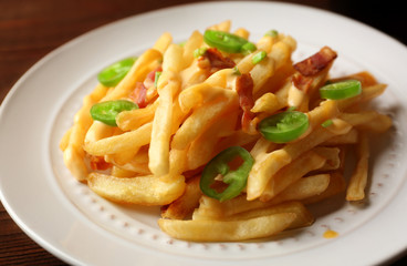 Tasty fries with cheese sauce and sliced pepper on plate