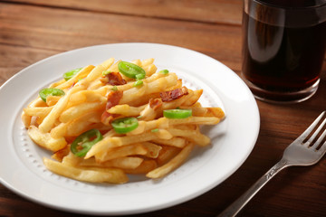 Plate with tasty cheese fries and glass of soda water on wooden table