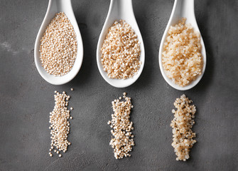 Three ceramic spoons with organic white quinoa grains on dark background