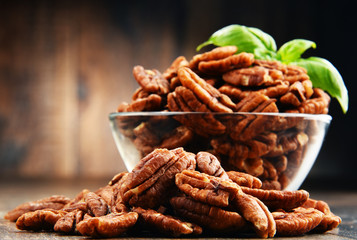 Bowl with pecan nuts on wooden table.