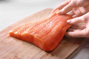 Hands putting fresh salmon fillet on wooden cutting board