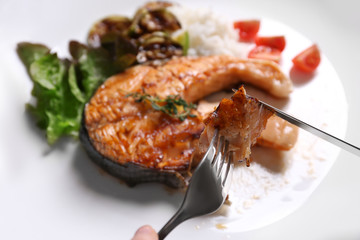 Tasting of grilled salmon steak with vegetables on white plate