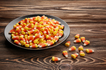 Plate with tasty Halloween candies on wooden background