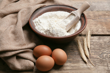 Bowl with flour, eggs and scoop on wooden table