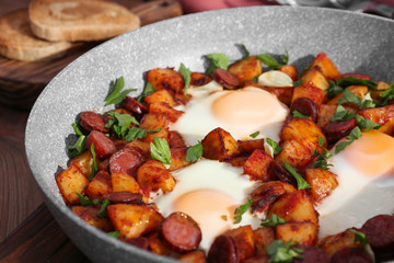 Baked eggs with sausages and potato in pan, closeup