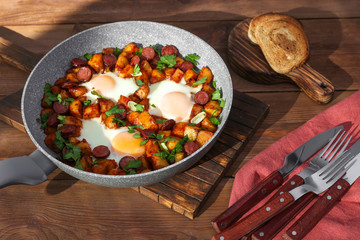 Baked eggs with sausages and potato on wooden table