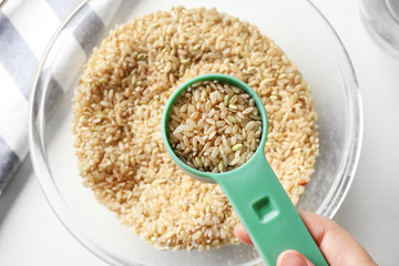 Measure scoop full of brown rice taken from glass bowl