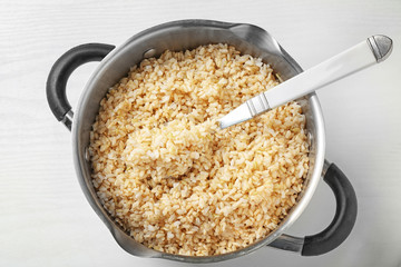 Pan with boiled brown rice on white background