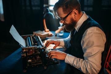 Bearded journalist in glasses typing on typewriter © Nomad_Soul