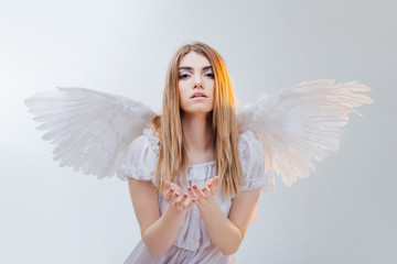 An angel from heaven holding something on the palms. Young, wonderful blonde girl in the image of an angel with white wings.