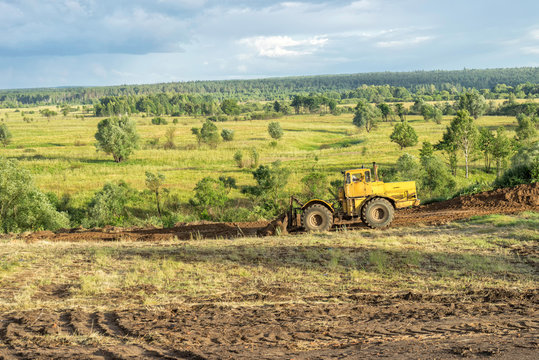 Wheeled tractor flattens area against sunny landscape. Bulatovo village, Kaluzskaya region, Russia.
