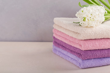 Stack of colorful bath towels with hyacinth flower on light background.