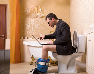 Man in glasses with laptop sitting on toilet bowl