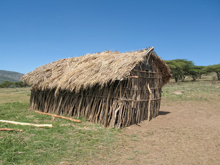Fototapeta na wymiar Small Maasai stockade village school sink to one side under thatched roof on flat meadow. Serengeti National Park, Tanzania, Africa. 