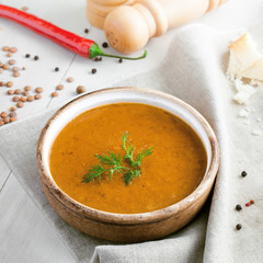 Lentil soup in a rustic bowl and a piece of bread on a cotton canvas tablecloth. Healthy vegetarian food on a white wooden table.
