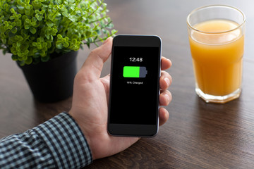 man hand holding phone with charged battery screen in office