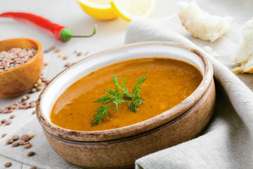 Healthy vegetarian lentil soup in a rustic clay bowl on a white wooden table. Delicious healthy meal served on a canvas tablecloth. Close-up shot.