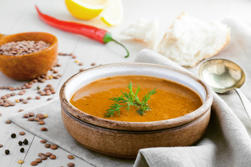 Bowl of delicious lentil soup with bread and lemon slice on a white wooden table. Traditional healthy vegetarian food.