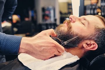 Stylish barber grooming a man's beard in a saloon.