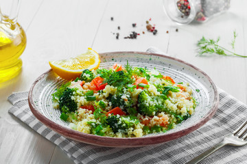 Vegetarian salad made of couscous, broccoli, tomato, pepper, onion and dill on a plate. Traditional Moroccan food for healthy meal on a table.