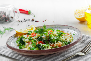 Plate with couscous and vegetables on a rustic wooden table. Traditional eastern healthy meal made of couscous, broccoli, tomato, pepper, onion and dill.