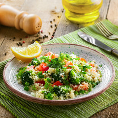 Plate with couscous and vegetables on a rustic wooden table. Traditional eastern healthy meal made of couscous, broccoli, tomato, pepper, onion and dill.