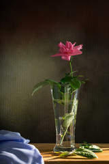 Pink roses in the glass and purple cloth on the wooden plate