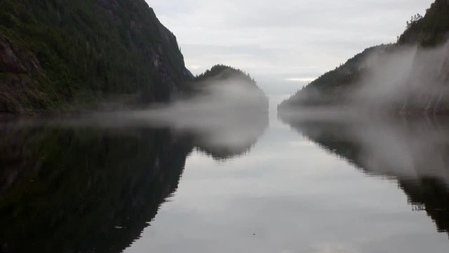 Mountains in fog on background of calm water in Pacific Ocean. Amazing landscapes. Beautiful rest and tourism in a cool climate. Unique picture of nature in America.