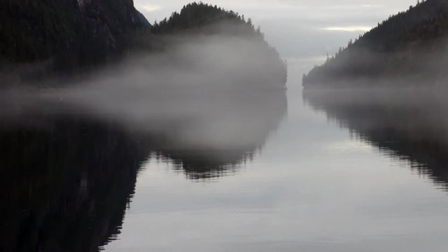Mountains in fog on background of calm water in Pacific Ocean. Amazing landscapes. Beautiful rest and tourism in a cool climate. Unique picture of nature in America.