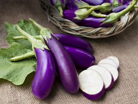 Raw violet eggplant in a wicker basket on sackcloth.