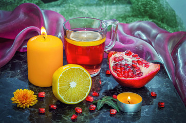 Fruit tea in a glass cup, lemon, pomegranate, burning candles on a marble surface