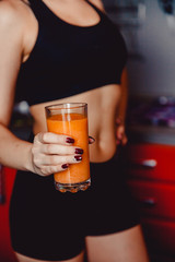 Sporty girl holding fresh carrot juice in a glass. Dark background.