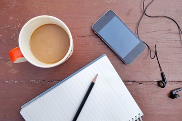 Wooden desk table with a cup of coffee, notebook,pen,clock. Top view with copy space, flat lay.