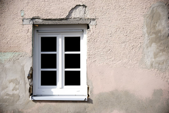 Hausrenovierung / Die Fassade eines renovierungsbedürftigen Hauses mit neu eingesetztem Fenster.