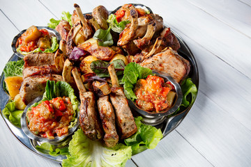 Meat plate with delicious pieces of meat, salad, ribs, grilled vegetables, potatoes and sauce on white wooden table