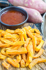 Healthy baked sweet potato fries on wooden board served with spicy sauce, vertical