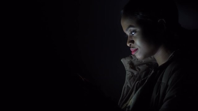 Black woman cheks her phone in the darkness