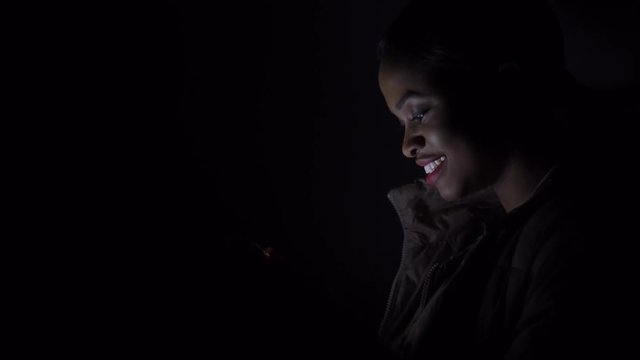 Black woman cheks her phone in the darkness