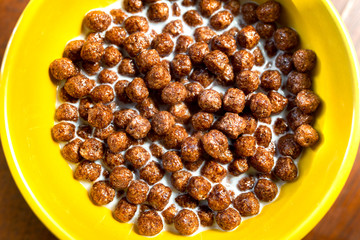 Traditional breakfast cereal chocolate balls with milk in a yellow plate.